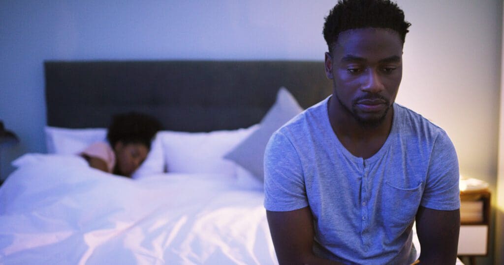 A man sitting in bed with his head on the pillow.