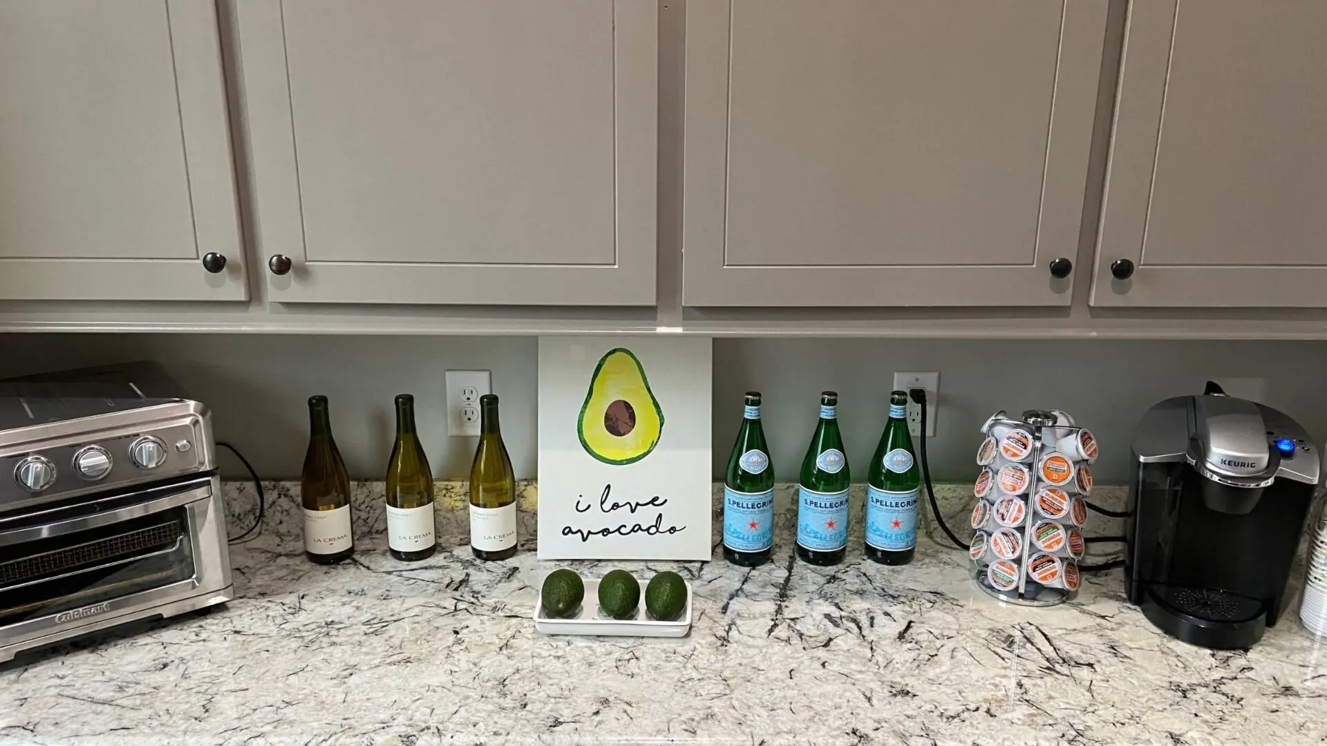 A counter with several bottles of wine and two avocados.